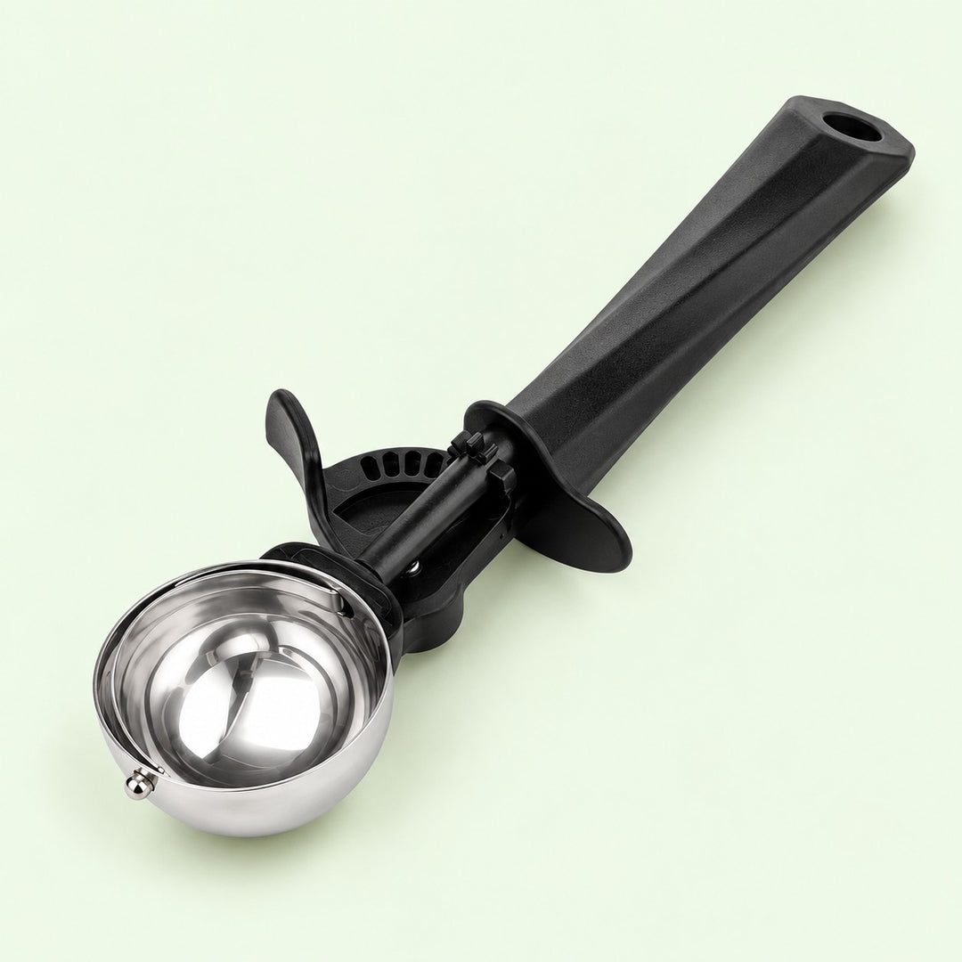 Small ice cream scoop with polished steel bowl and black handle on a pale green backdrop.
