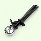 Smallest ice cream scoop with polished steel bowl and black handle on a pale green backdrop.
