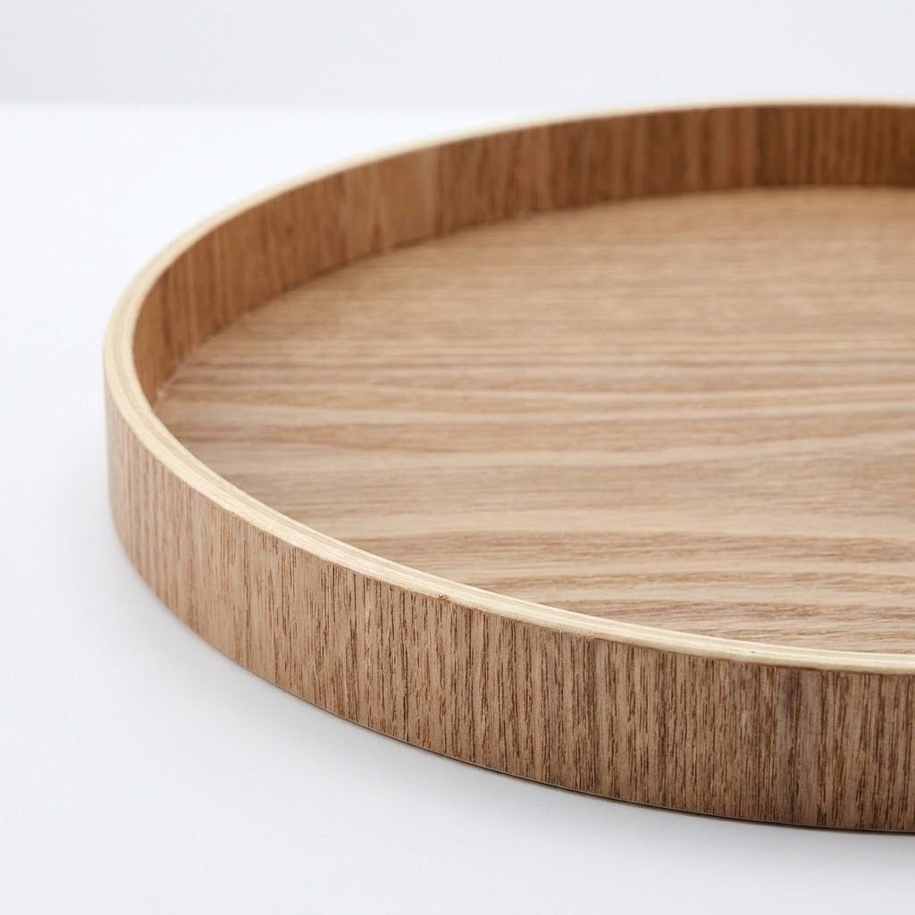 A close-up of a round wooden tray with a light natural wood grain finish and a smooth rim, shown on a clean white background.