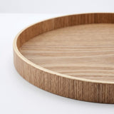 A close-up of a round wooden tray with a light natural wood grain finish and a smooth rim, shown on a clean white background.