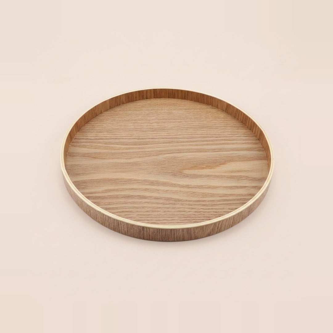 A round wooden tray with a smooth, light-colored wood-grain top and a contrasting darker brown rim, shown on a solid, warm off-white background.