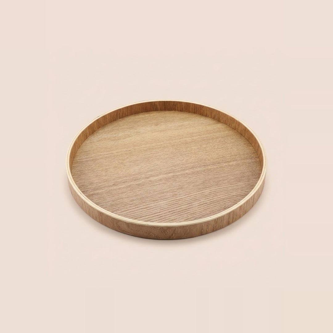 A round wooden serving tray with a natural light oak finish and visible wood grain, shown from a top-down perspective on a solid, warm off-white background.