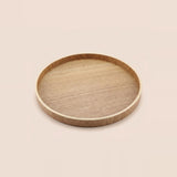 A round wooden serving tray with a natural light oak finish and visible wood grain, shown from a top-down perspective on a solid, warm off-white background.