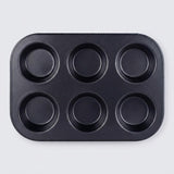 A black non-stick six-cup muffin tin with a rectangular base and six round cups, photographed from directly above on a light gray background.
