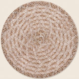 A round braided placemat with a textured spiral pattern in beige and brown, shown on a solid light cream background.