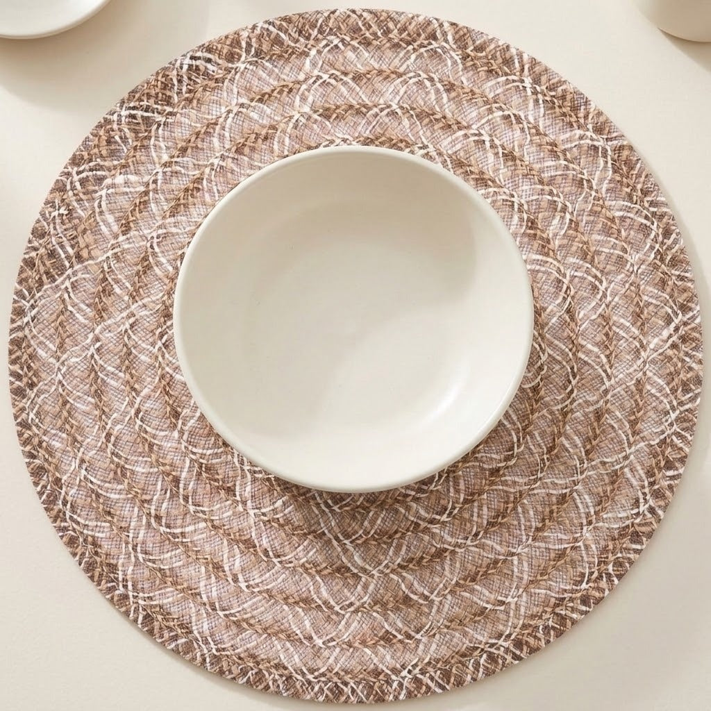 A round woven placemat in beige and white with a textured basketweave pattern, styled with a white ceramic bowl in the center on a light cream tabletop.
