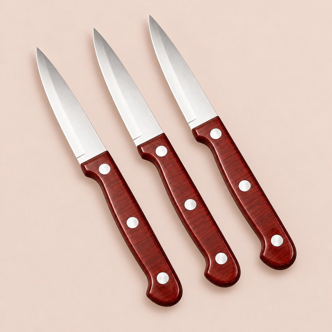 Three stainless steel paring knives with reddish three-rivet handles on a soft rose backdrop.
