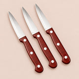Three stainless steel paring knives with reddish three-rivet handles on a soft rose backdrop.