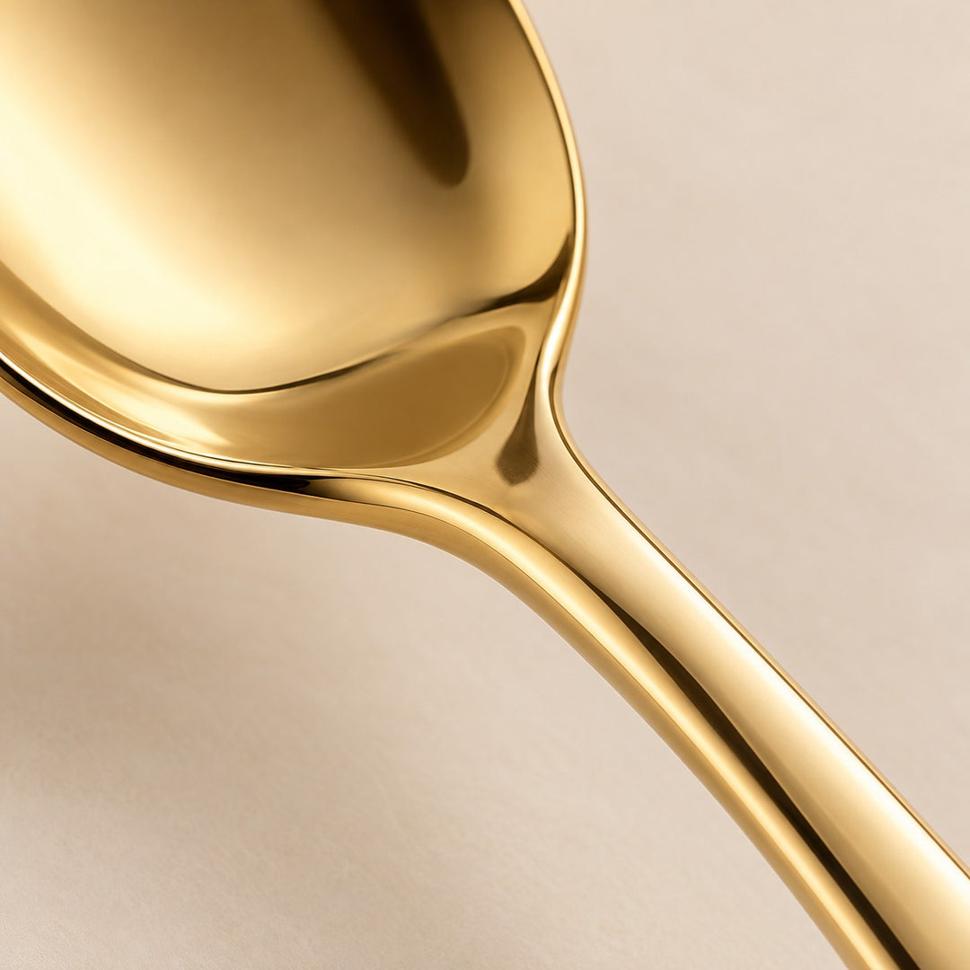 A macro view shows the smooth reflective gold finish of the stainless steel spoon and handle.