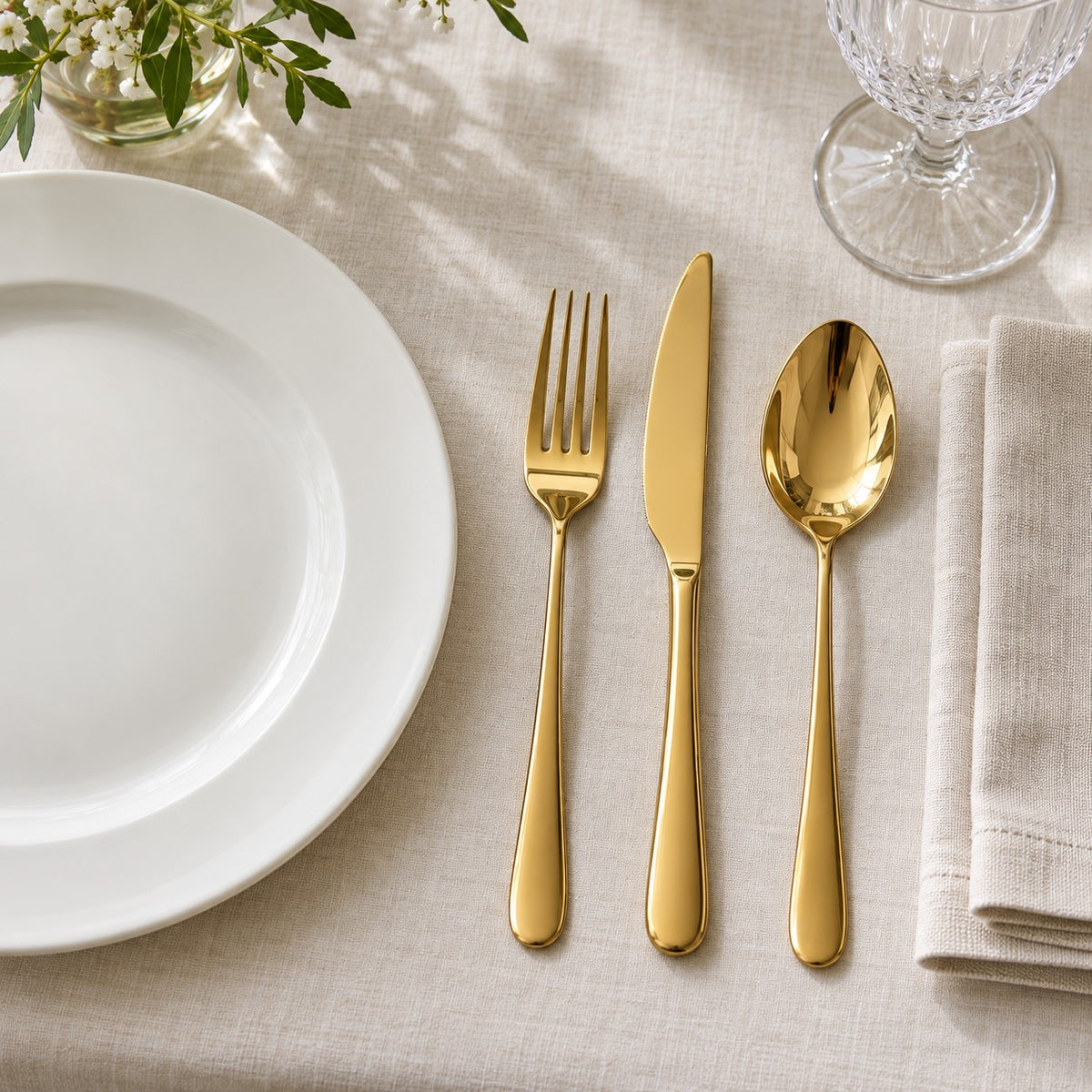 A gold stainless steel knife, fork and spoon sit beside a dinner plate to show their table scale.