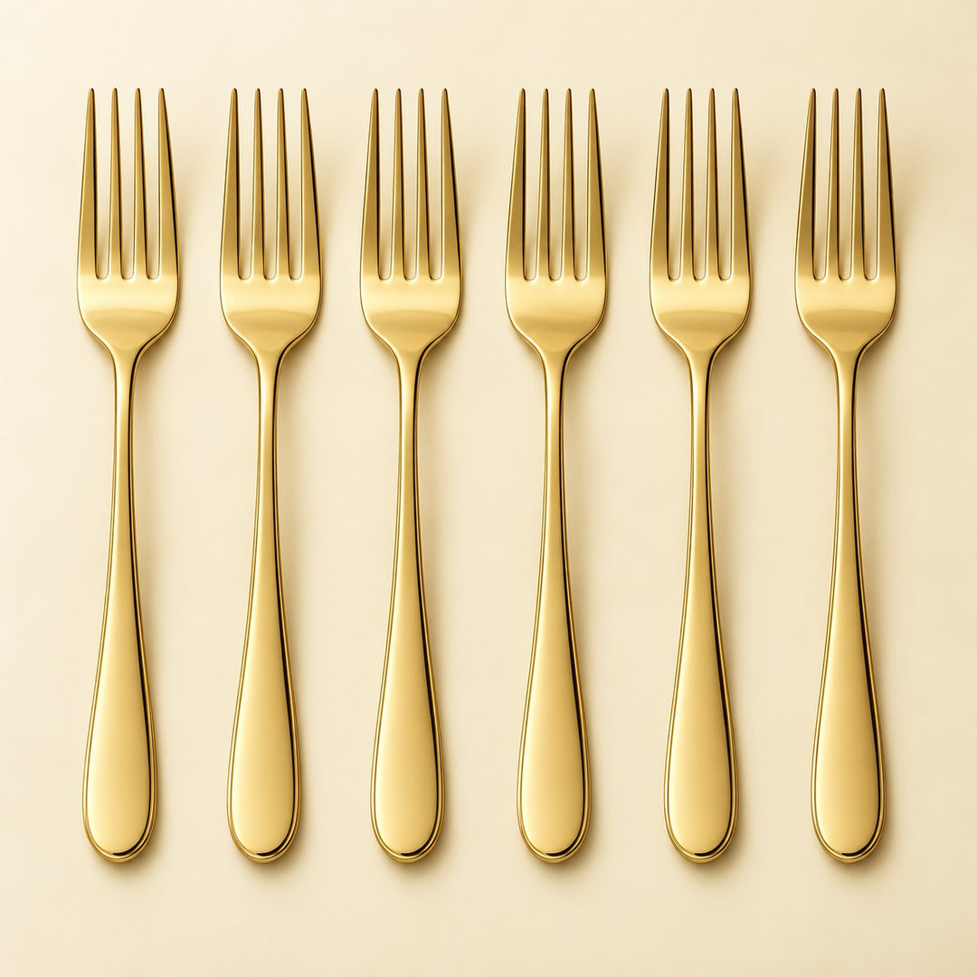 Six polished gold stainless steel dinner forks are arranged in a row on a pale backdrop.