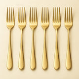 Six polished gold stainless steel dinner forks are arranged in a row on a pale backdrop.