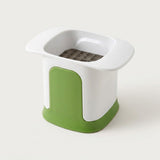 A kitchen utensil with a white plastic body and a green base, featuring a square grid filter or strainer inside a recessed top opening, set against a plain light background.