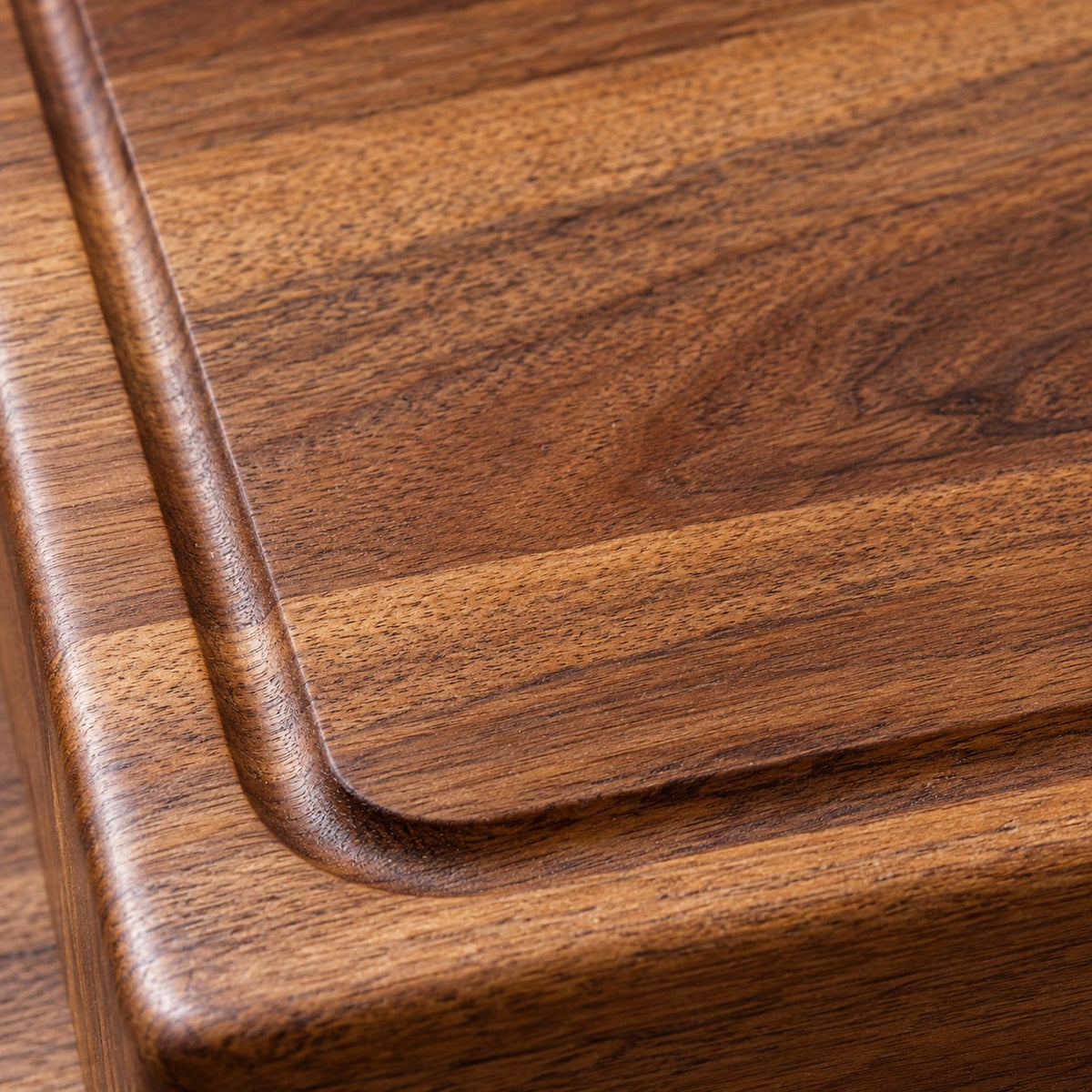 A macro view of the wood cutting board reveals its warm grain, smooth finish, and carved groove.