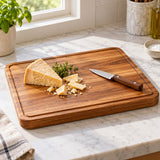 A rectangular wood cutting board holds cheese on a bright kitchen counter during meal preparation.