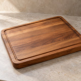 A warm brown wood cutting board shows its recessed perimeter groove and rounded edges in a close hero view.