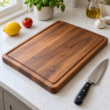 A rectangular wood cutting board sits beside a lemon, tomato, and chef knife on a kitchen counter.
