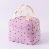 A light pink gingham-patterned lunch bag with a brown floral print and cream-colored handles, shown on a light lavender background.