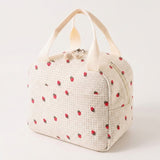 An off-white woven lunch bag with a red strawberry pattern and cream-colored top handles, shown on a plain light background.