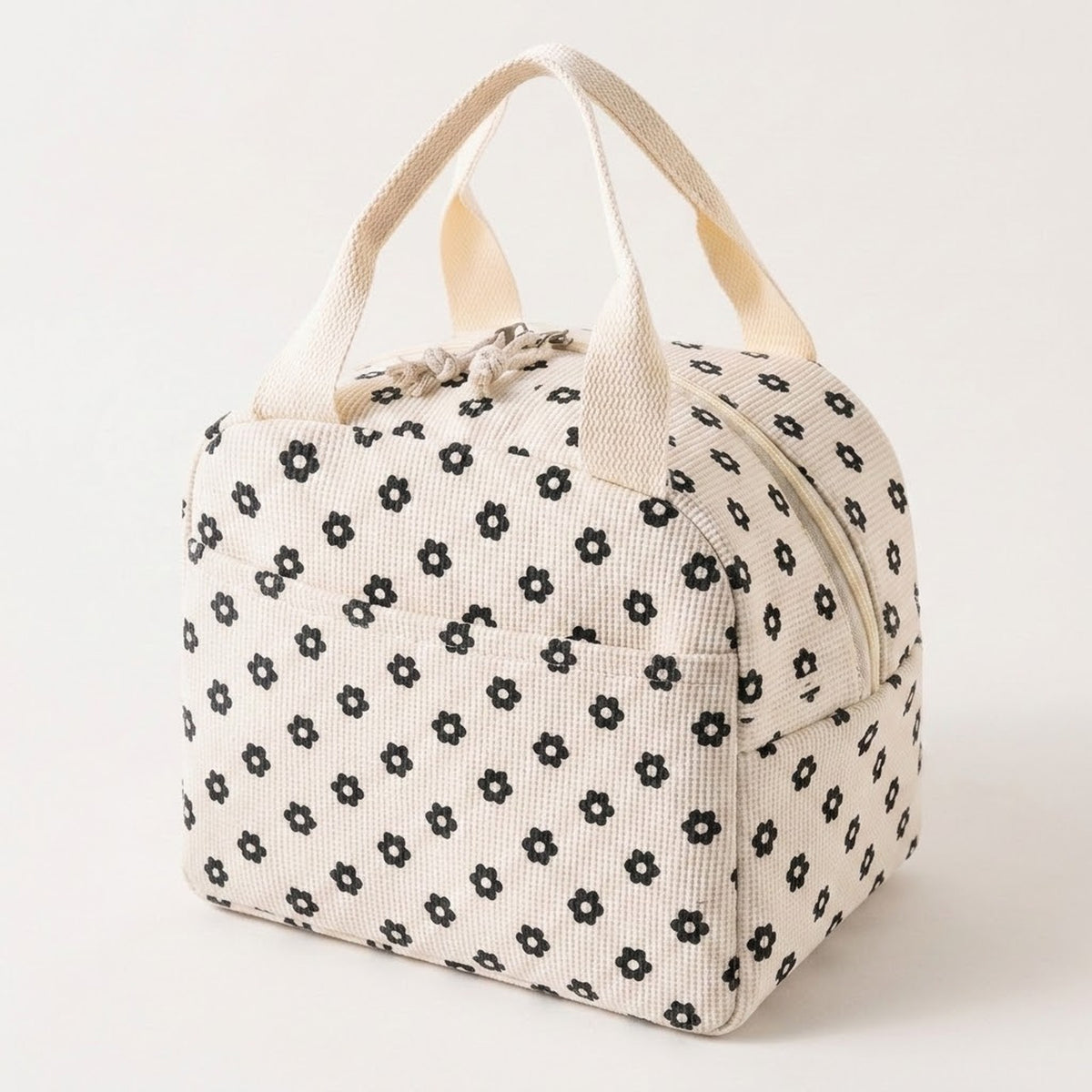 An off-white canvas lunch bag with a black floral pattern and cream-colored handles, photographed on a clean white background.