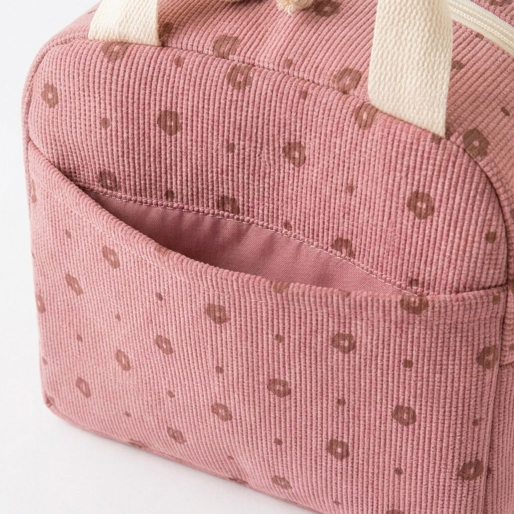 A close-up of a pink ribbed corduroy bag with a repeating brown polka dot pattern and cream-colored fabric handles.
