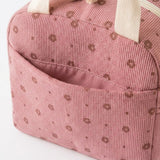 A close-up of a pink ribbed corduroy bag with a repeating brown polka dot pattern and cream-colored fabric handles.