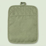 An olive green quilted fabric pot holder with a top loop handle and a horizontal seam creating a front pocket, shown against a solid pale green background.