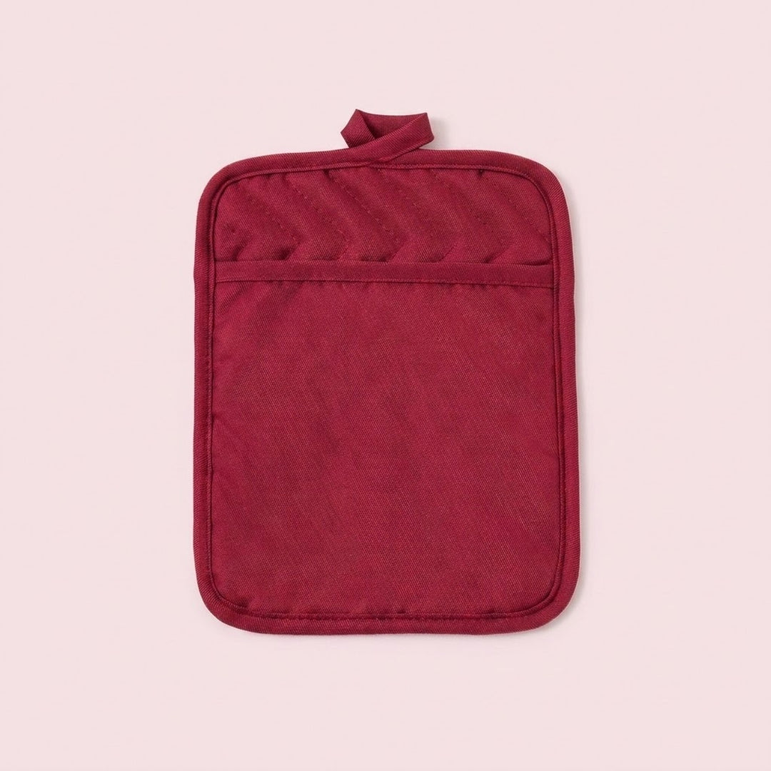 A single deep red quilted pot holder with a top loop handle, shown flat against a solid pale pink background.