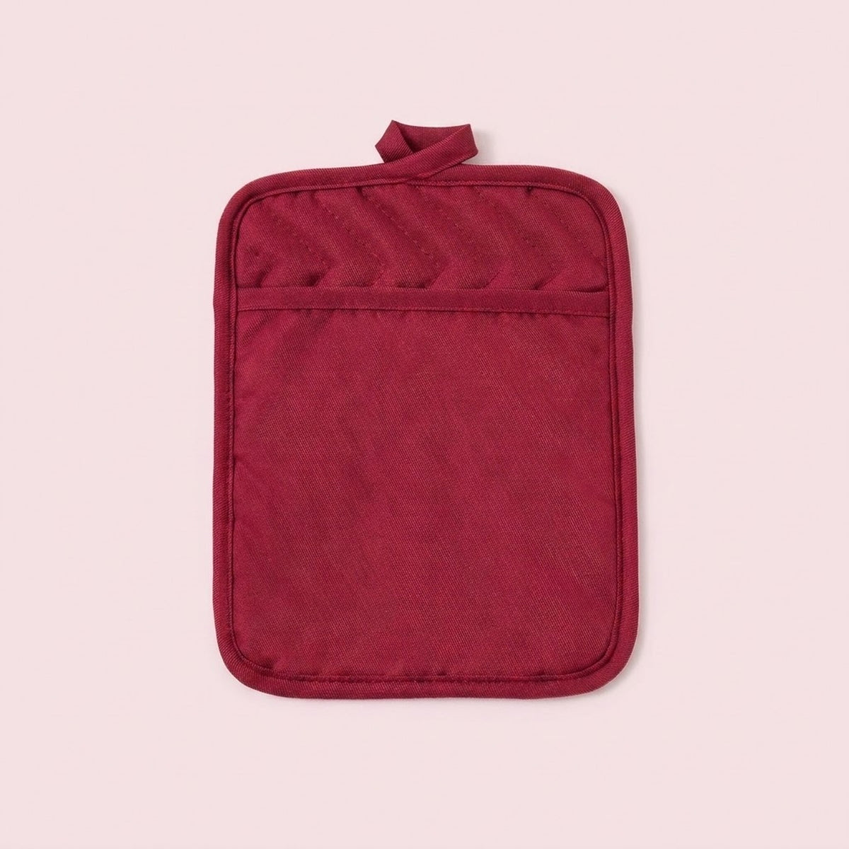A single deep red quilted pot holder with a top loop handle, shown flat against a solid pale pink background.