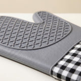 A gray silicone oven mitt with a textured non-slip grip and a black-and-white gingham checkered fabric wrist strap, shown on a light beige background.