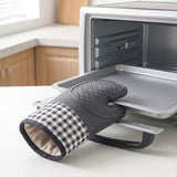 A black and gray quilted oven mitt with a black-and-white gingham cuff is shown resting on a white kitchen counter in front of an open microwave.