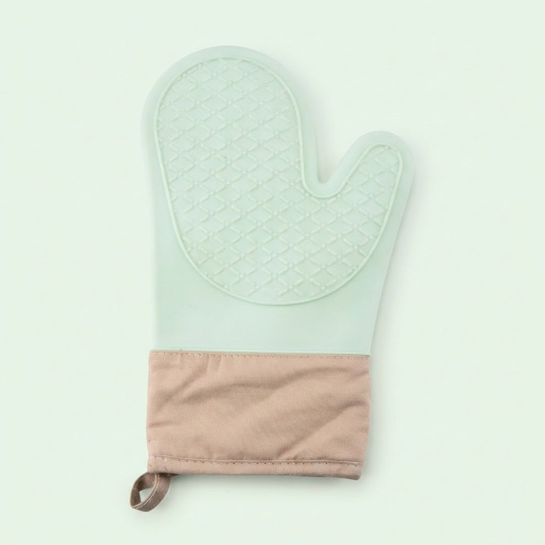 A quilted oven mitt in pale mint green with a textured diamond pattern on the palm side and a solid dusty pink fabric cuff at the bottom, featuring a small matching fabric loop.