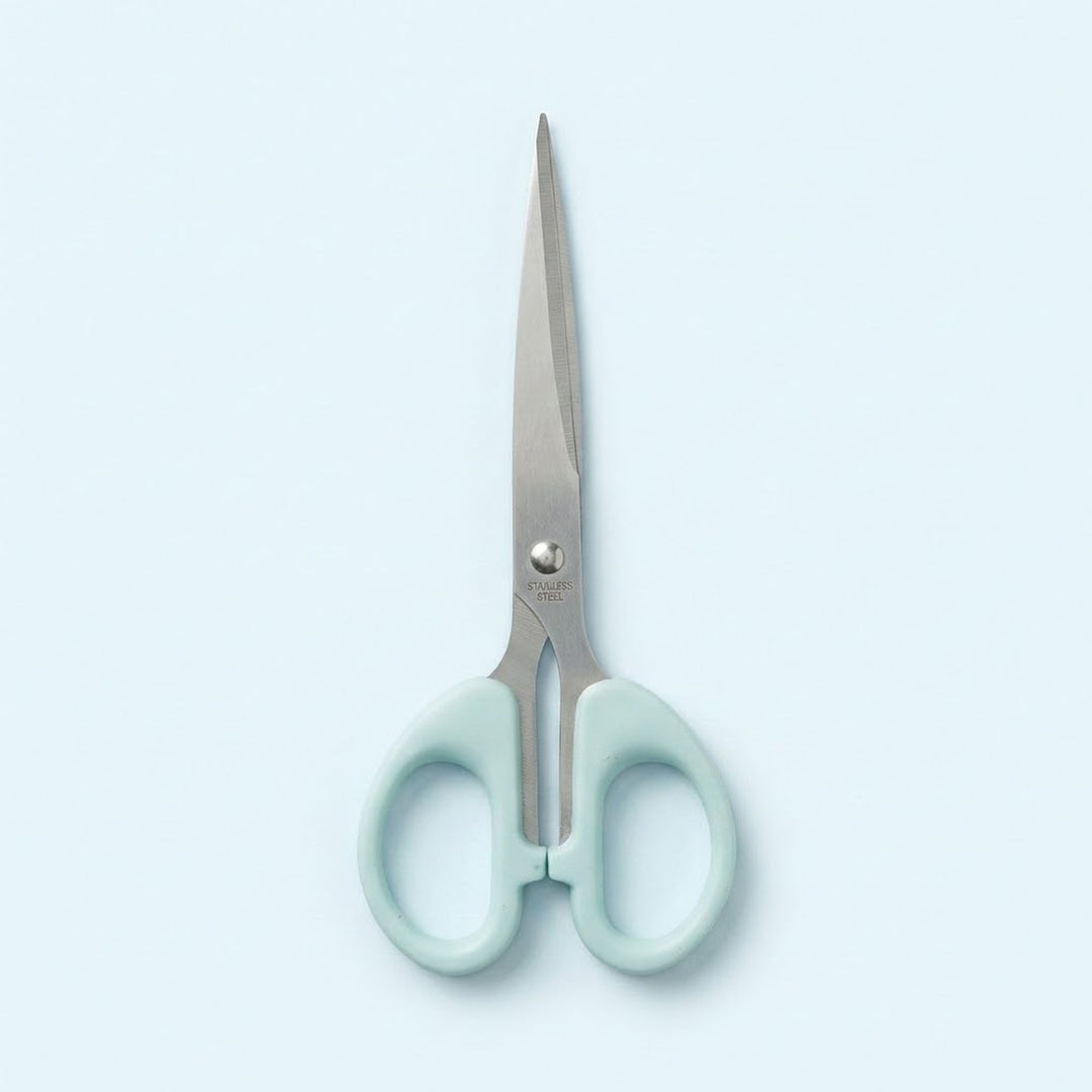 A pair of scissors with light mint green handles and silver stainless steel blades, centered on a pale blue background.