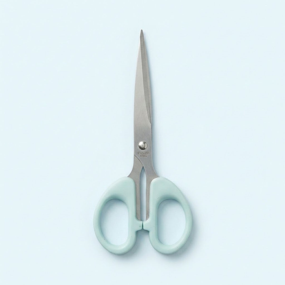 A pair of scissors with light mint green handles and silver stainless steel blades, centered on a pale blue background.