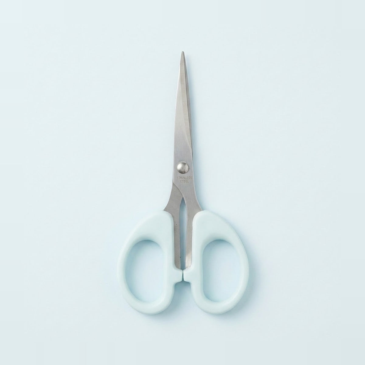 A pair of scissors with light blue handles and silver stainless steel blades, centered on a pale blue background.