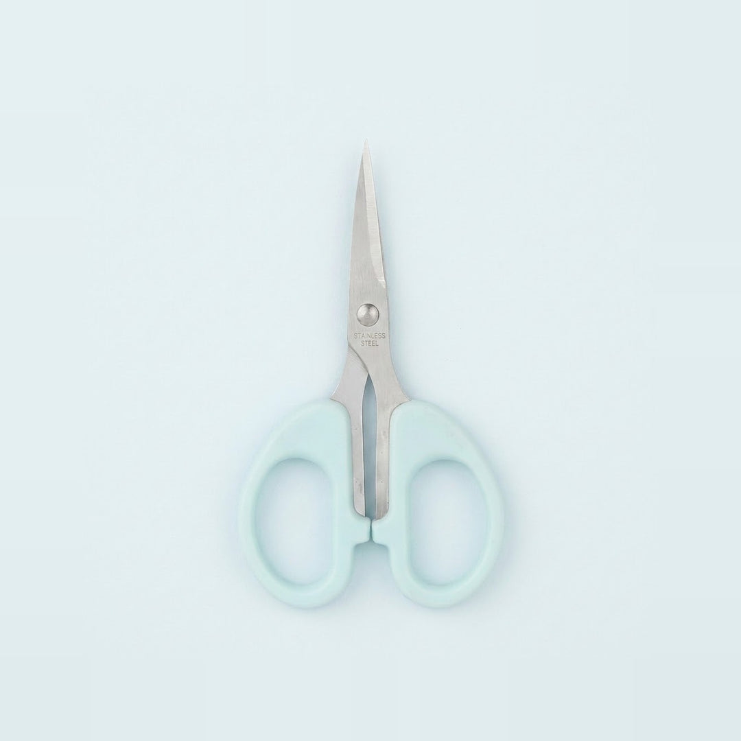 A pair of small scissors with pale mint green handles and silver stainless steel blades, centered on a clean, light blue background.