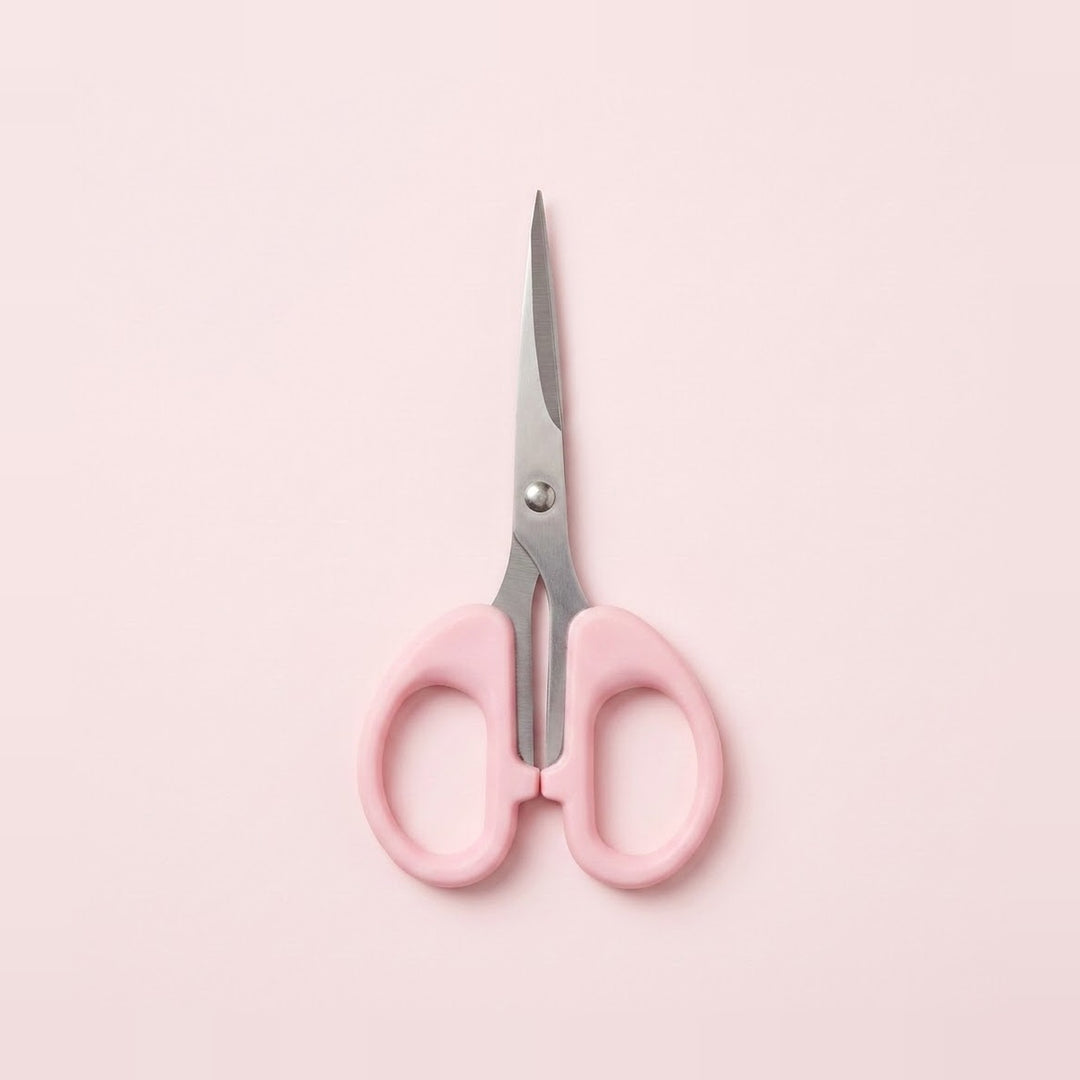 Pink-handled scissors with silver metal blades, centered on a solid pale pink background.