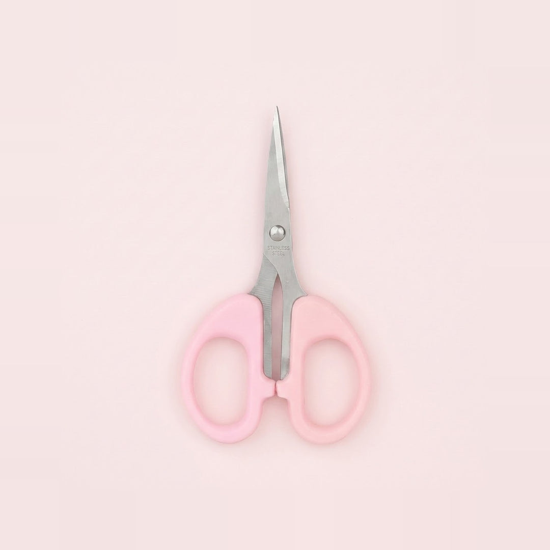 A pair of small scissors with light pink handles and silver metal blades, centered on a solid pale pink background.