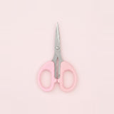 A pair of small scissors with light pink handles and silver metal blades, centered on a solid pale pink background.
