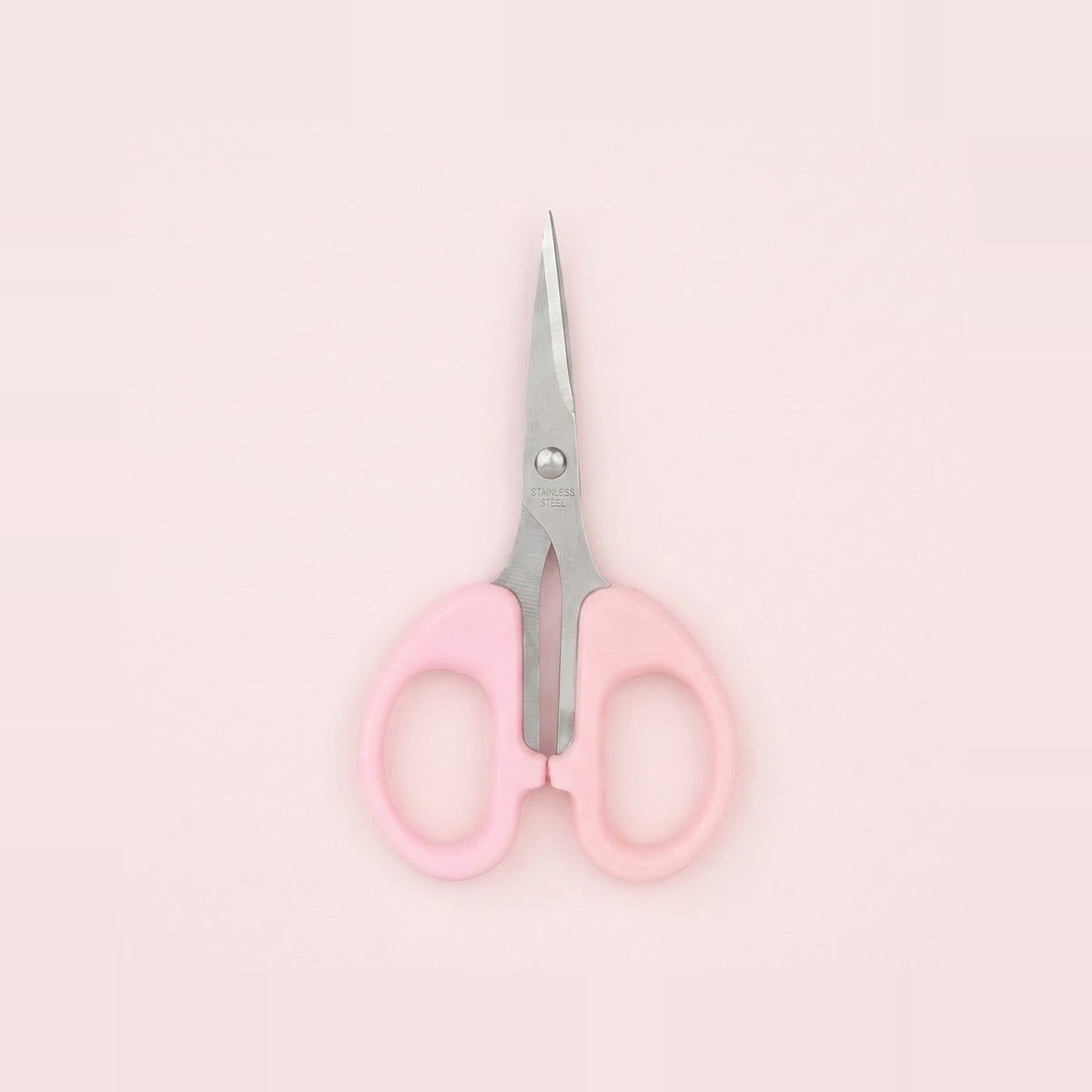 A pair of small scissors with light pink handles and silver metal blades, centered on a solid pale pink background.