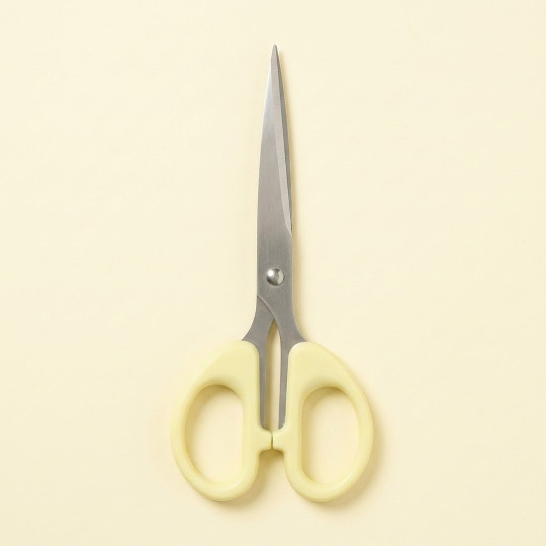 A pair of scissors with pale yellow handles and silver metal blades, centered on a solid cream-colored background.
