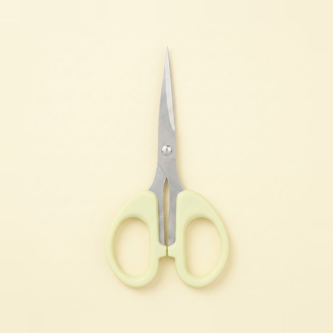 A pair of small scissors with pale yellow-green plastic handles and silver metal blades, centered on a solid cream-colored background.
