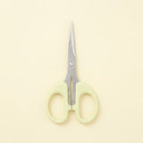A pair of small scissors with pale yellow-green plastic handles and silver metal blades, centered on a solid cream-colored background.