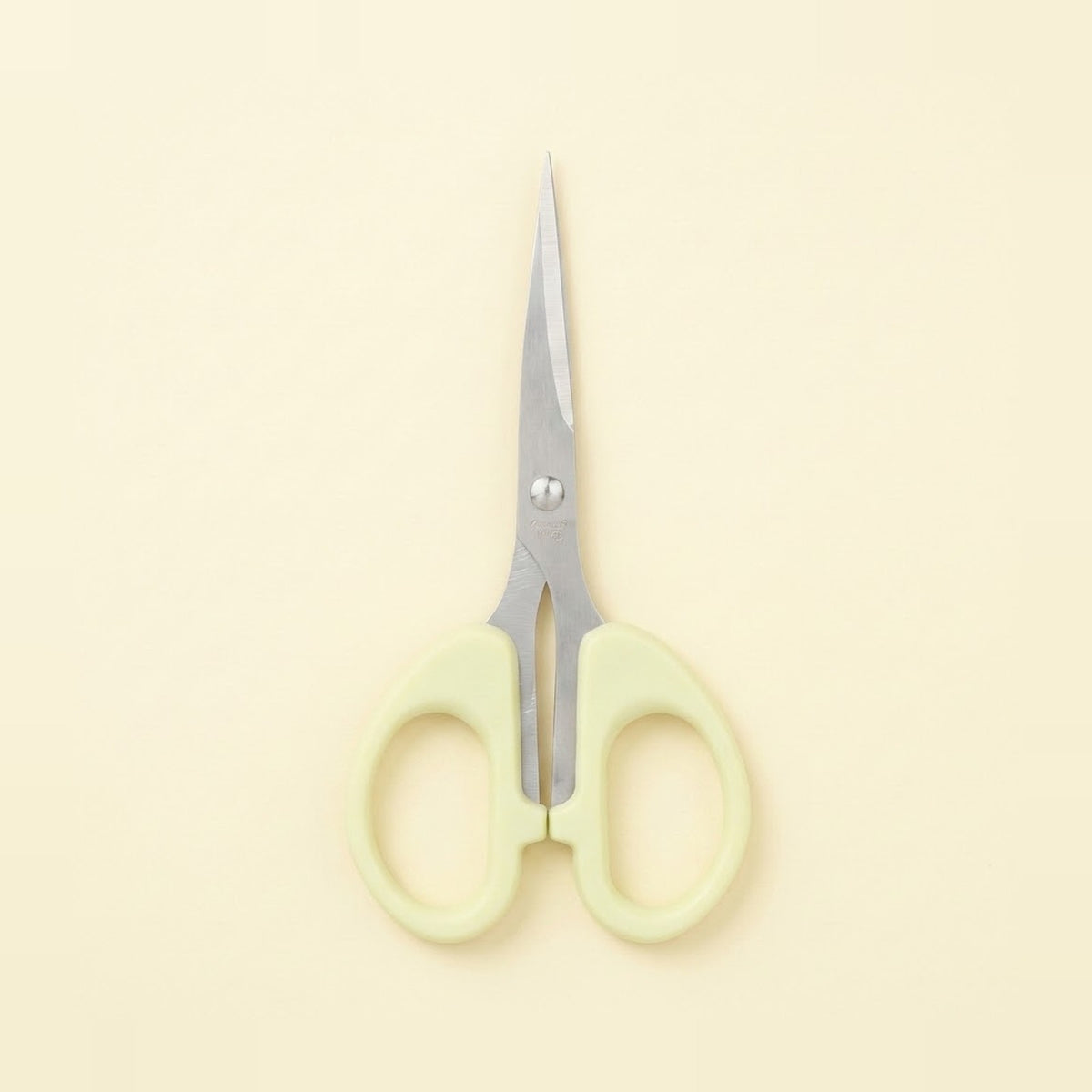 A pair of small scissors with pale yellow-green plastic handles and silver metal blades, centered on a solid cream-colored background.