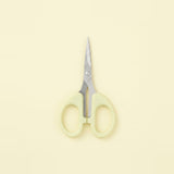 A pair of small scissors with pale yellow-green handles and silver metal blades, centered on a solid pale cream background.