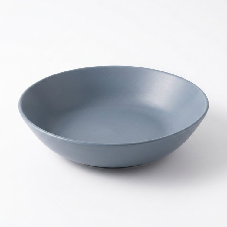 A matte slate blue ceramic bowl photographed from a high angle on a clean white background.