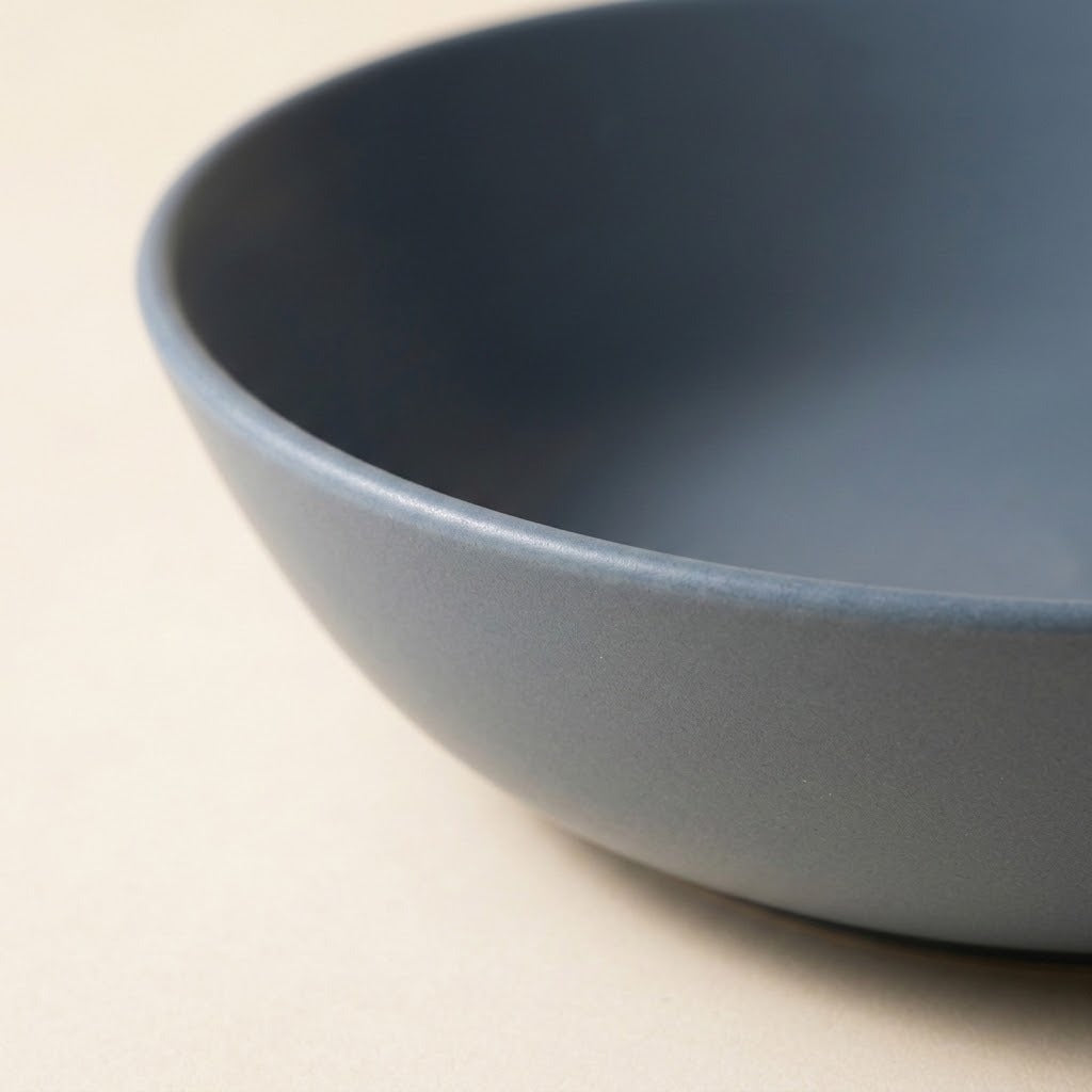 A close-up shot of a matte slate blue ceramic bowl on a light beige background.