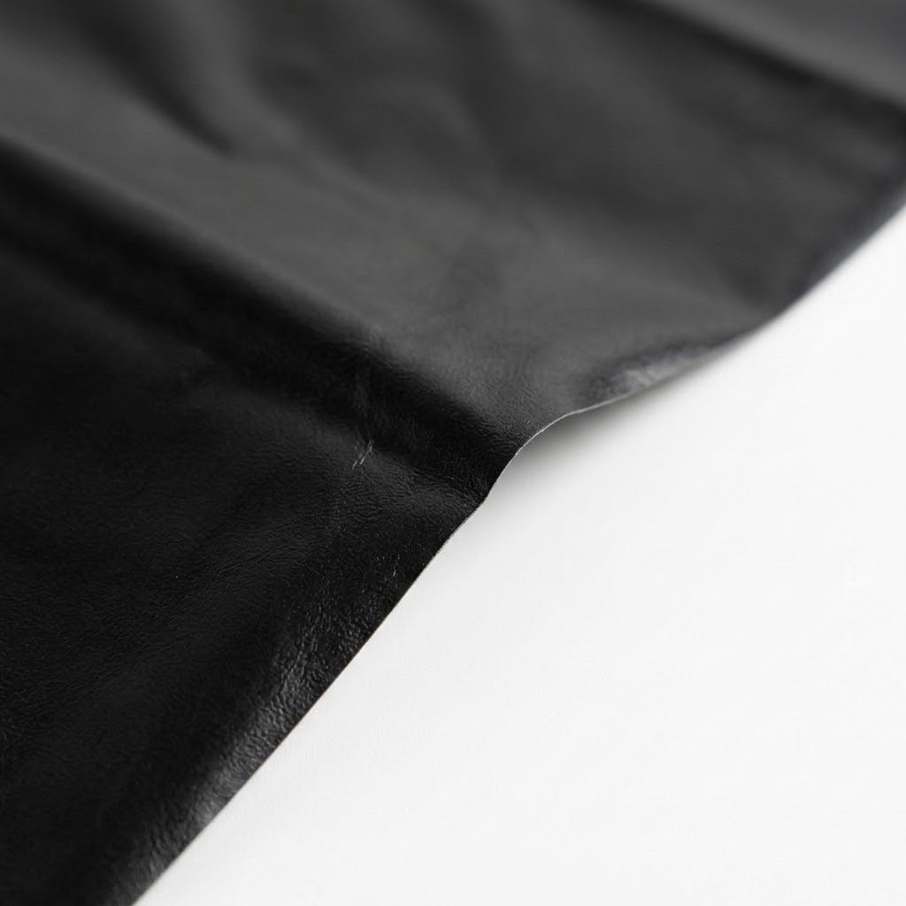A close-up of a black material, likely leather or faux leather, draped diagonally across a plain white surface.