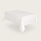 A plain white rectangular tablecloth draped over a table, shown against a light warm gray studio background.