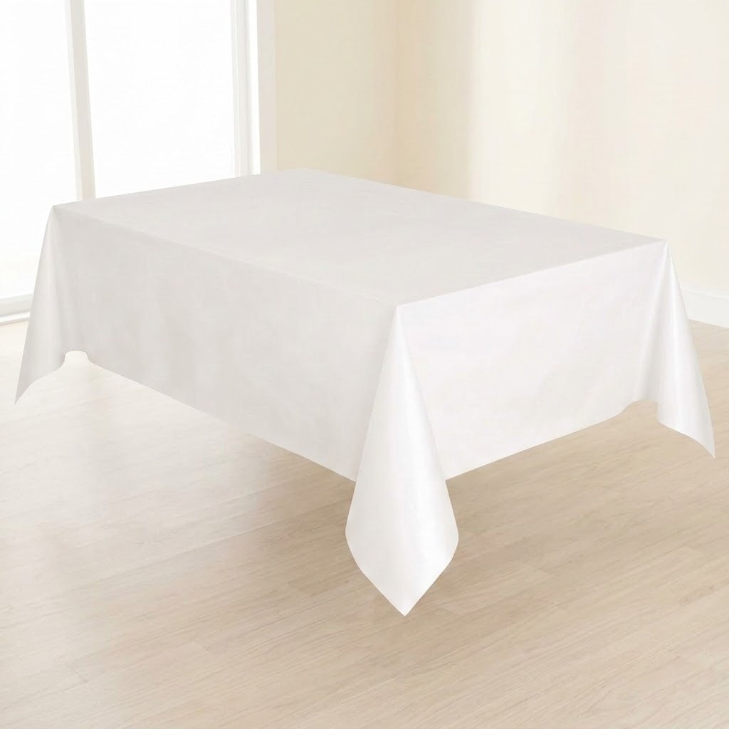 A plain white rectangular tablecloth draped over a table in a bright indoor room with light wood flooring and cream walls.
